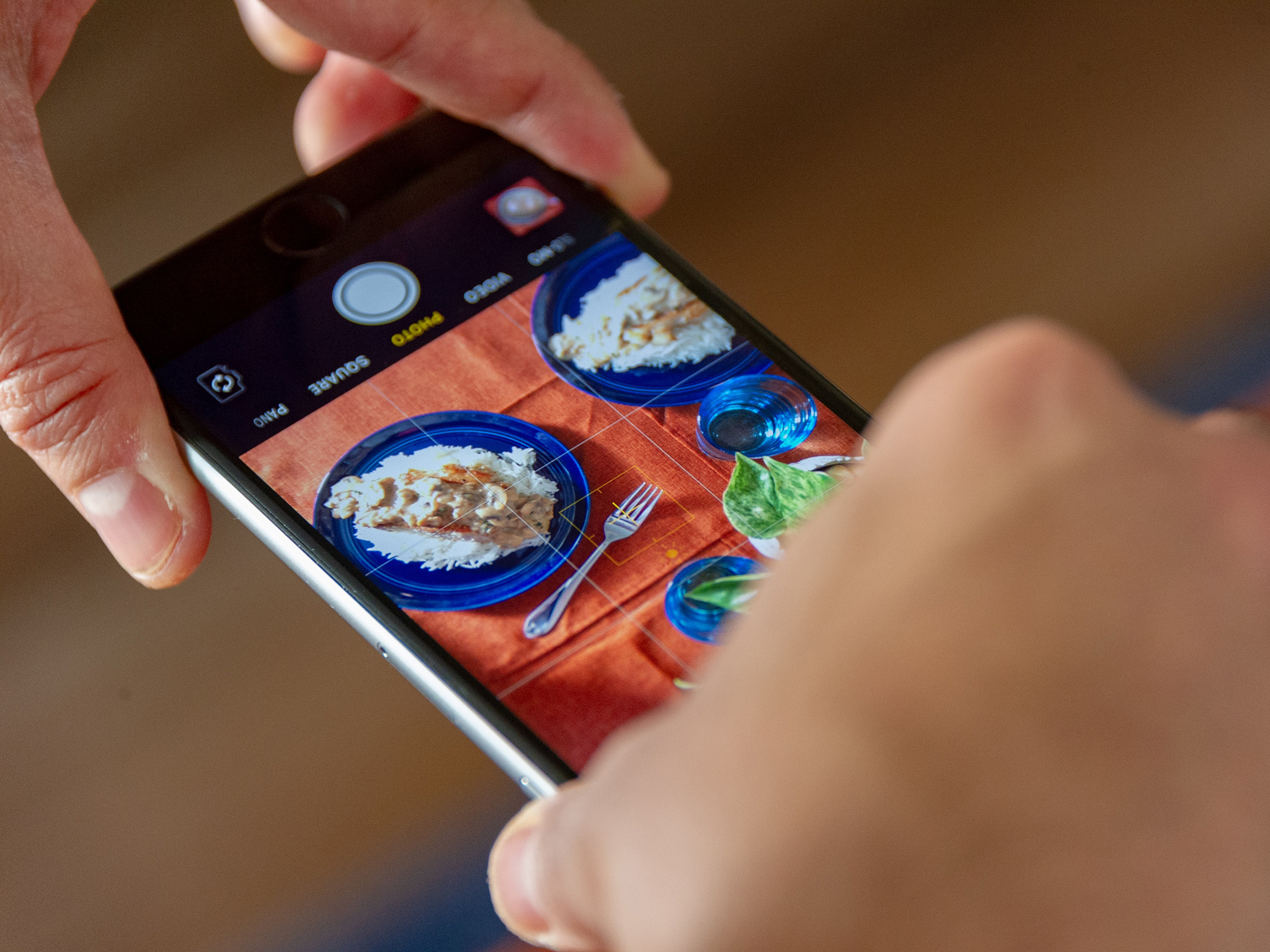 A person using their iPhone to take a photo of some food on a table.