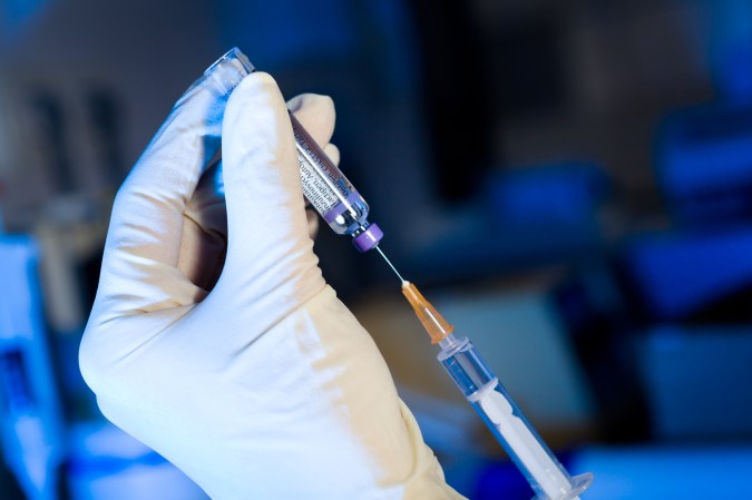 A gloved hand drawing a vaccine.