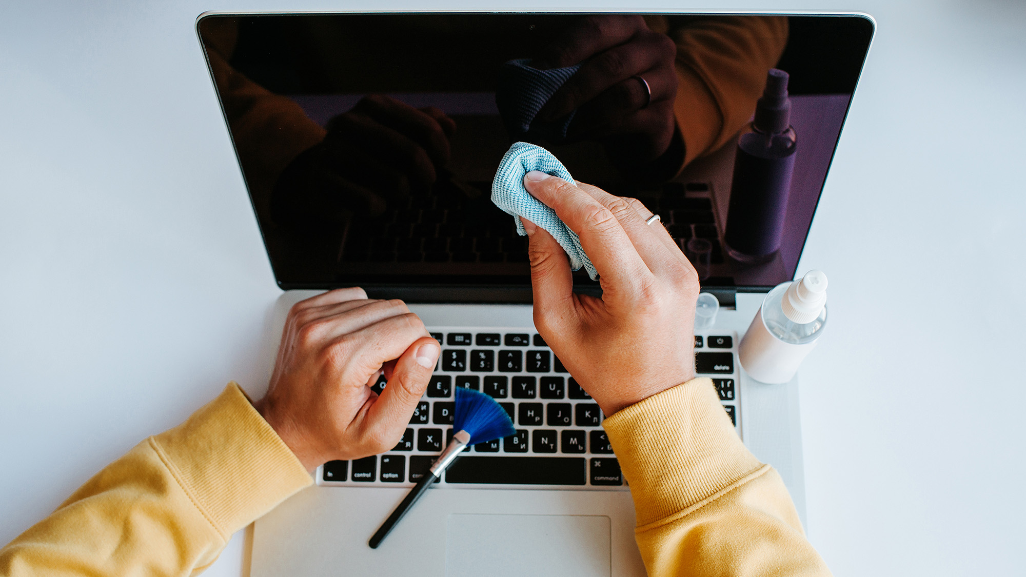 A person cleaning a laptop screen with a microfiber cloth and small brush.