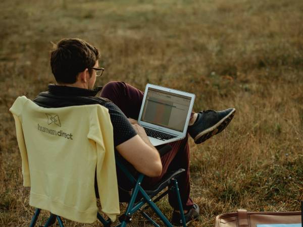 Person sitting on lawn chair with laptop working and looking out into a field