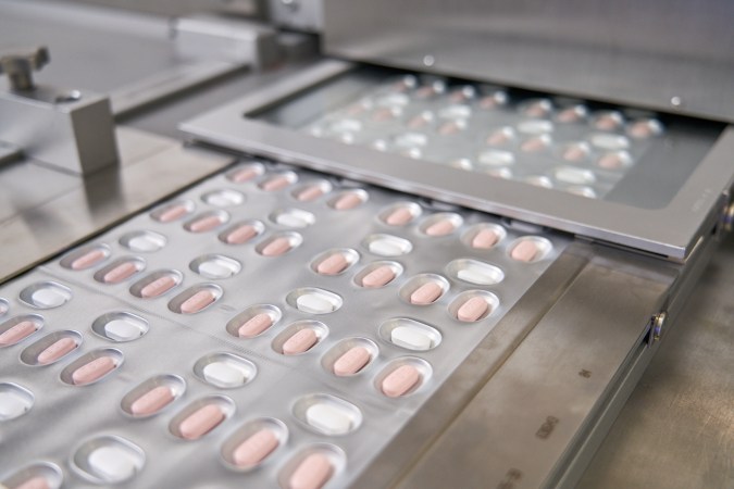 Three white and pink Pfizer COVID antiviral pills in plastic packaging.