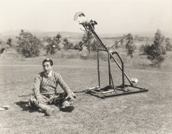 Automized putter comically dropping a golf ball on a person's head in a black and white image