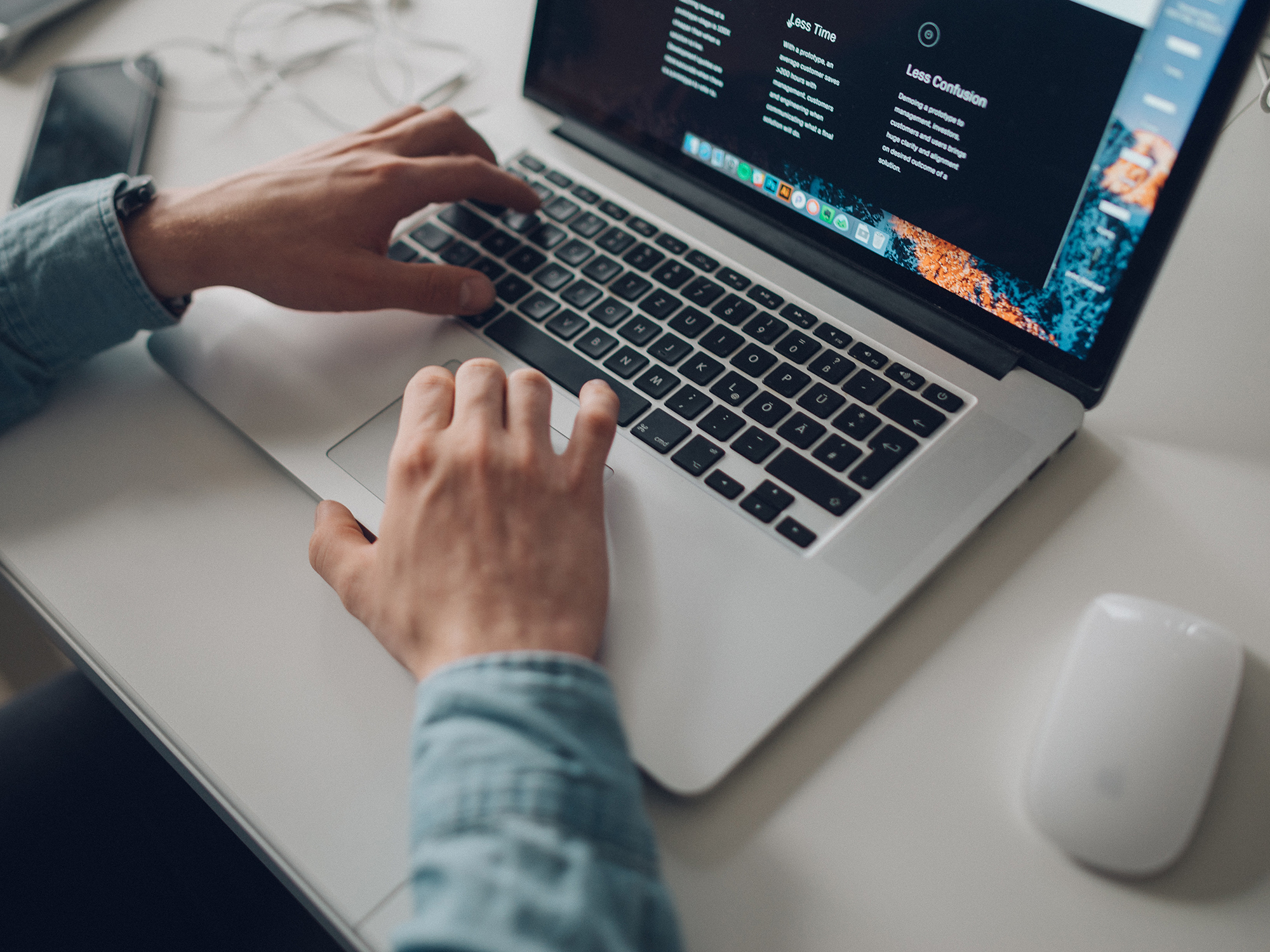 A person using a Macbook laptop on a white table.