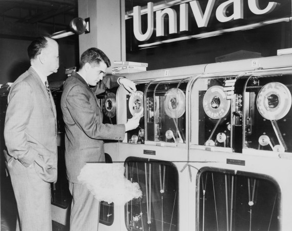 Two people in suits counting on a wall-size Univac computer in 1959 in a black and white photo