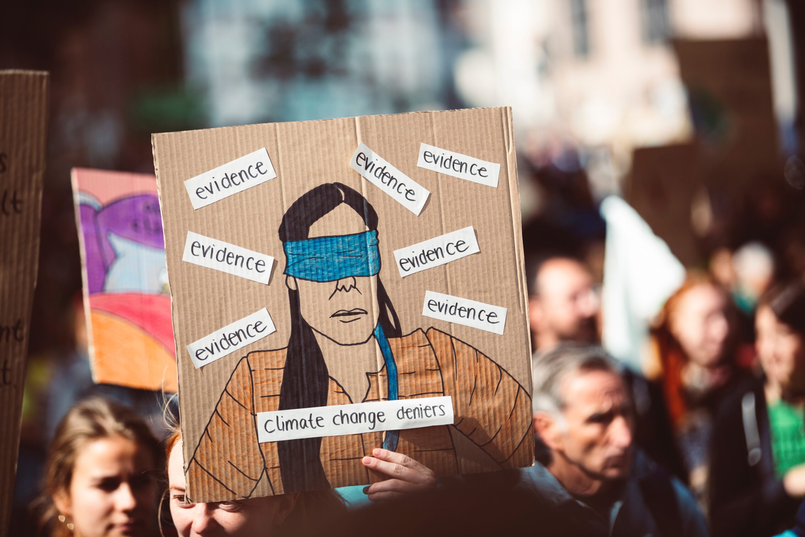 Climate change protest poster with blindfolded person surrounded by climate hoax buzz words