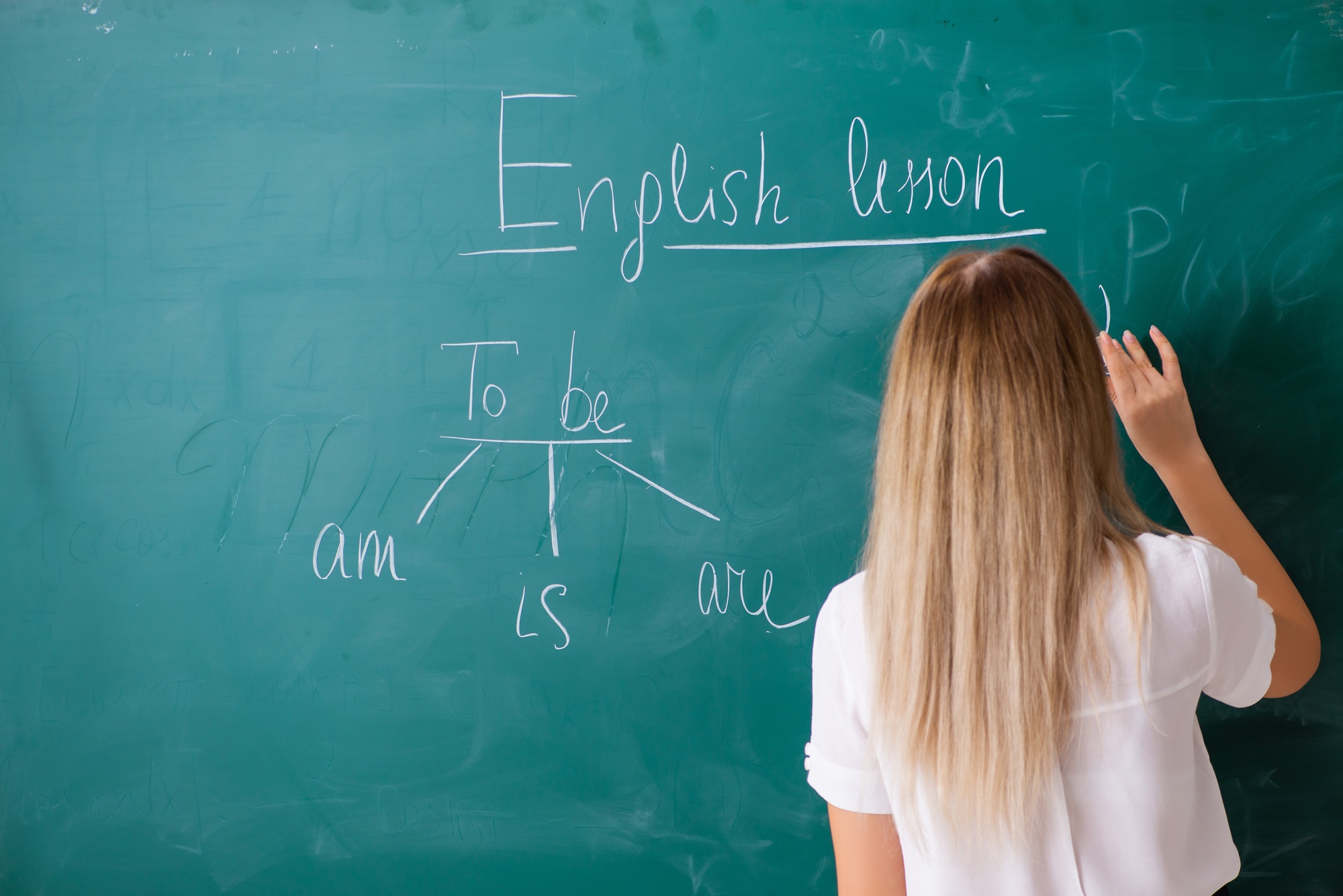 English teacher with long blonde hair at a chalkboard with grammar and words