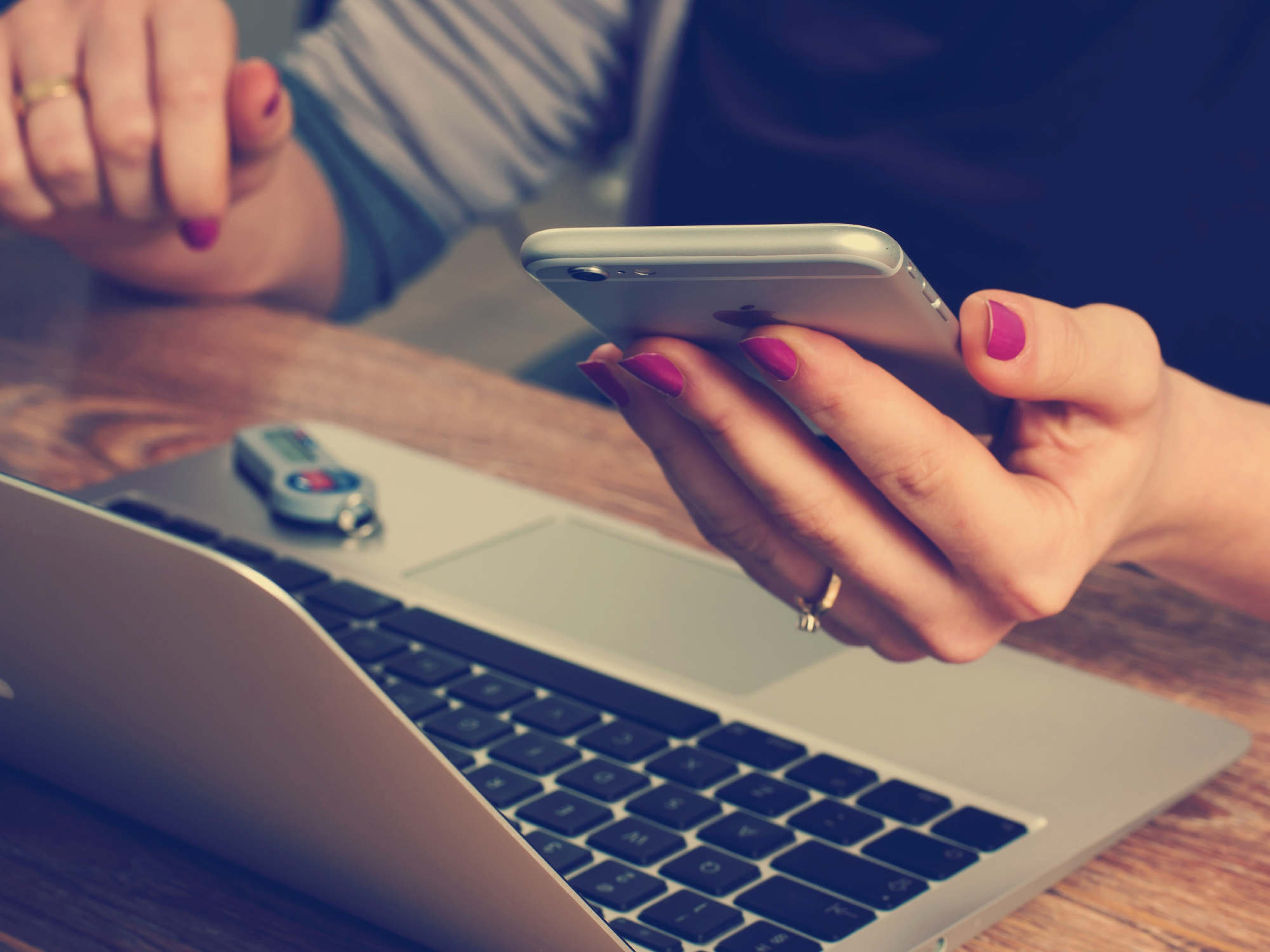 A woman with red nailpolish holding an iPhone and using a Macbook laptop to secure her online accounts.