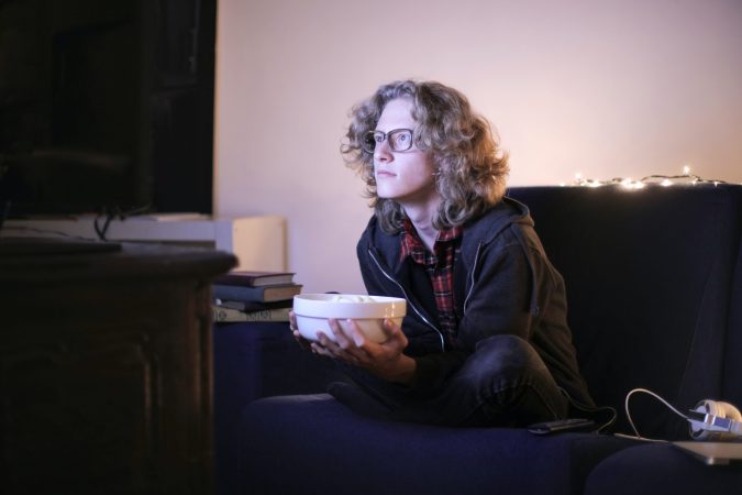 Person watching television with bowl of popcorn.