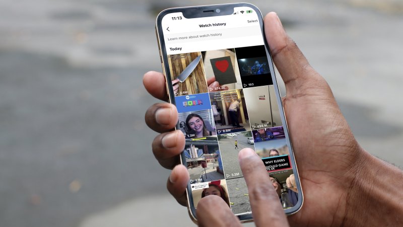A person holding an iPhone outside, looking at their TikTok watch history