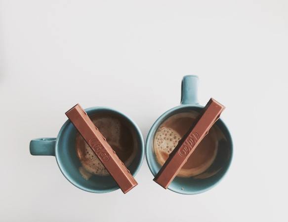 two pieces of a kit kat bar balanced on mugs of hot chocolate