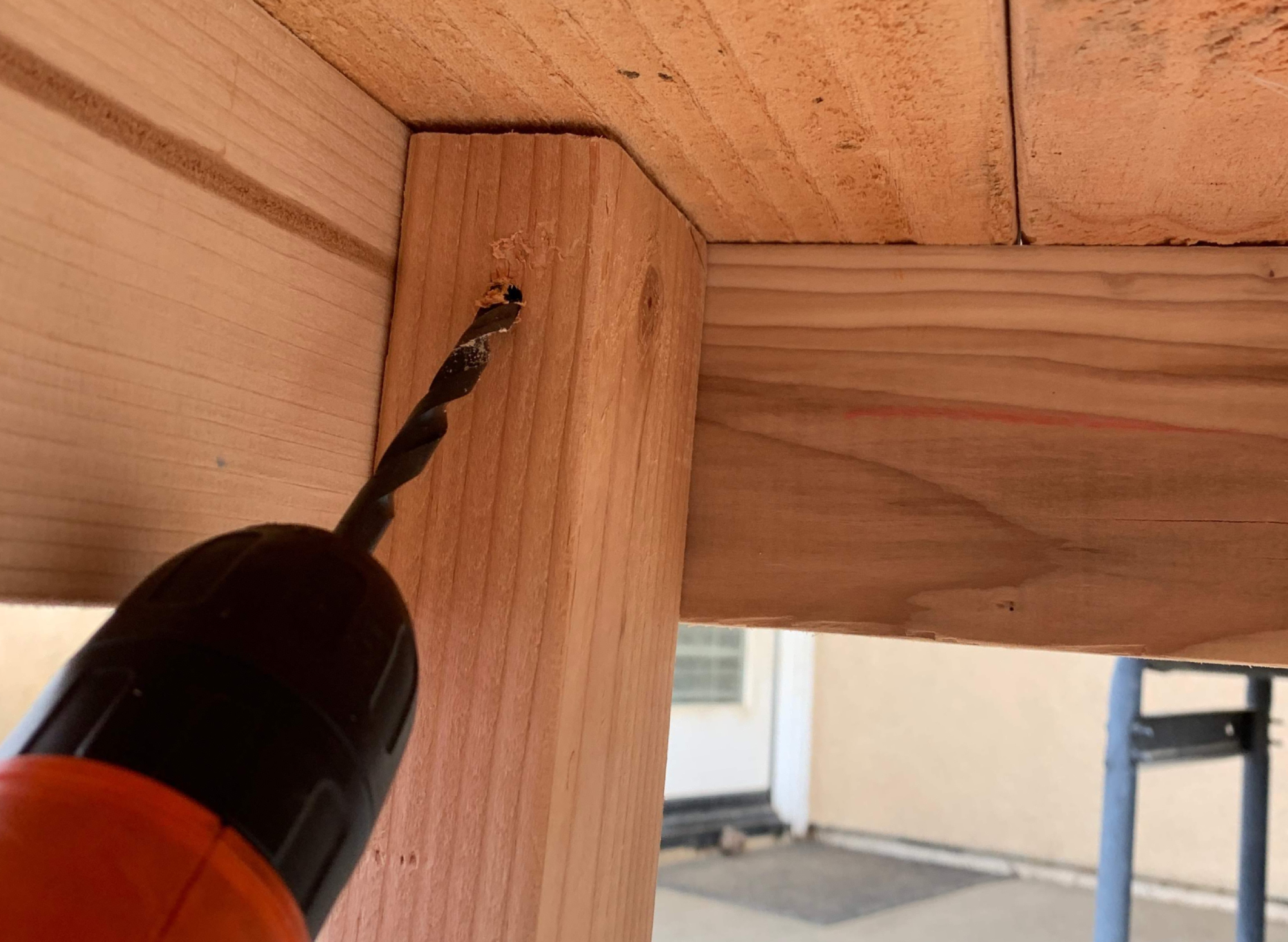 A person drilling at an upward angle into a table top on a wooden DIY shoe rack.