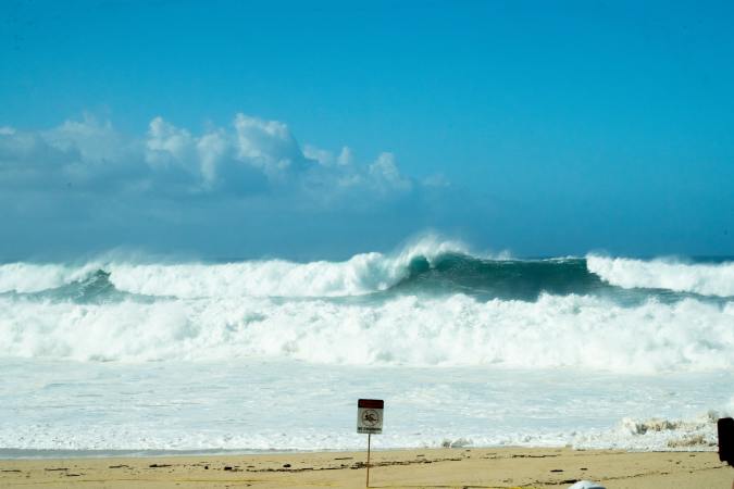 choppy waves on a beach with a sign warning people not to swim