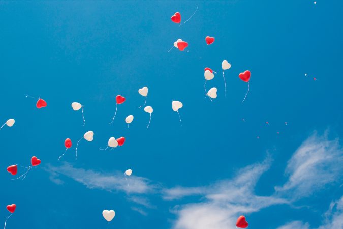 Red and white heart balloons released into blue sky which can become hazardous.