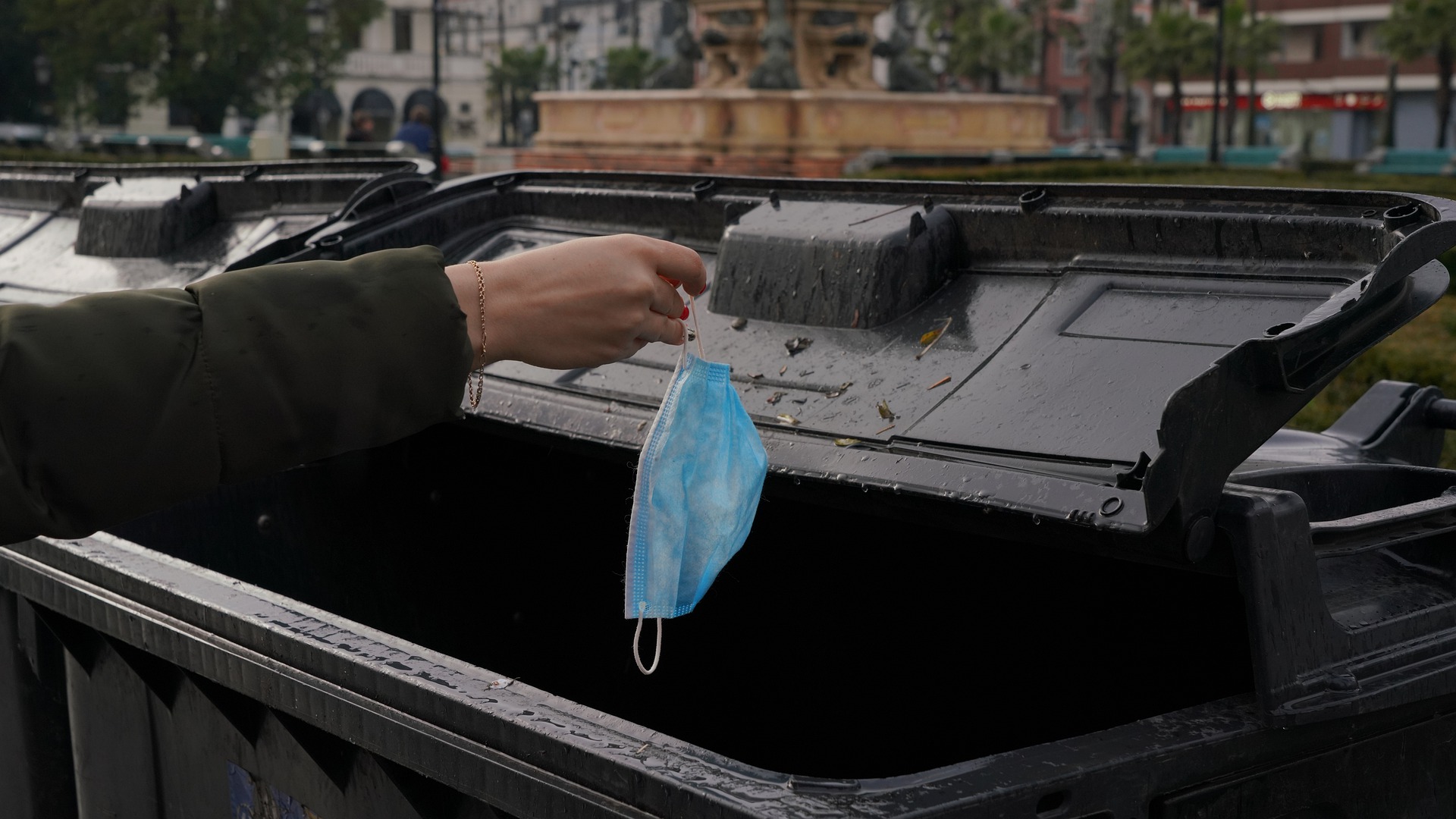 Person throwing COVID-19 disposable mask in trash can.