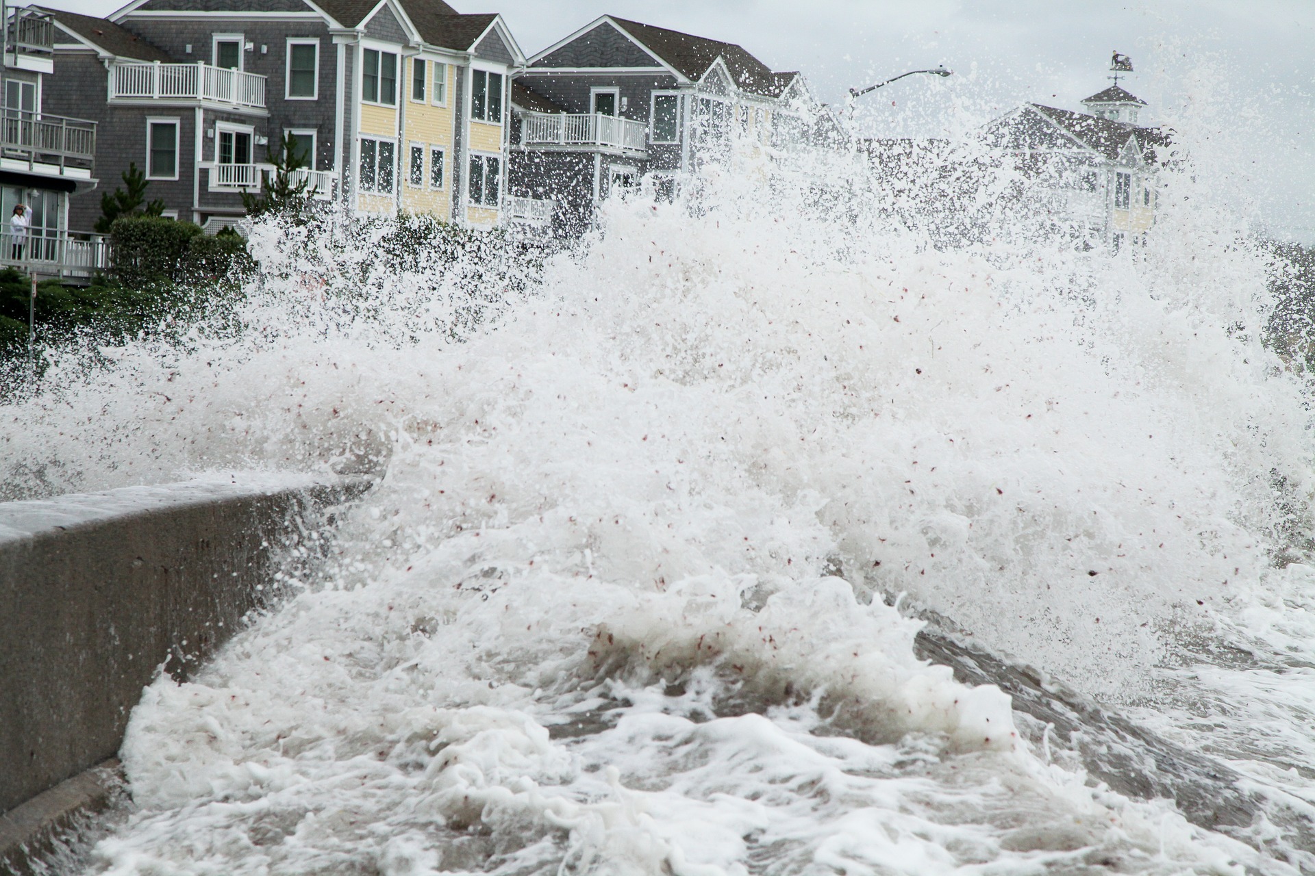 a violent wave crashes over a row of homes