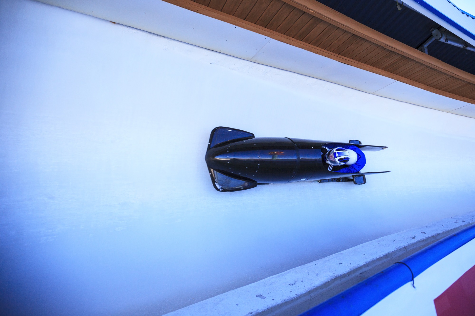 Blue multi-person bobsled speeding around a curve on an ice track