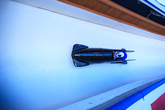 Blue multi-person bobsled speeding around a curve on an ice track