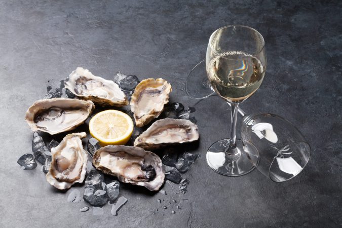 six raw oysters in a circle around a lemon next to a glass of champagne to be used as aphrodisiacs for sex