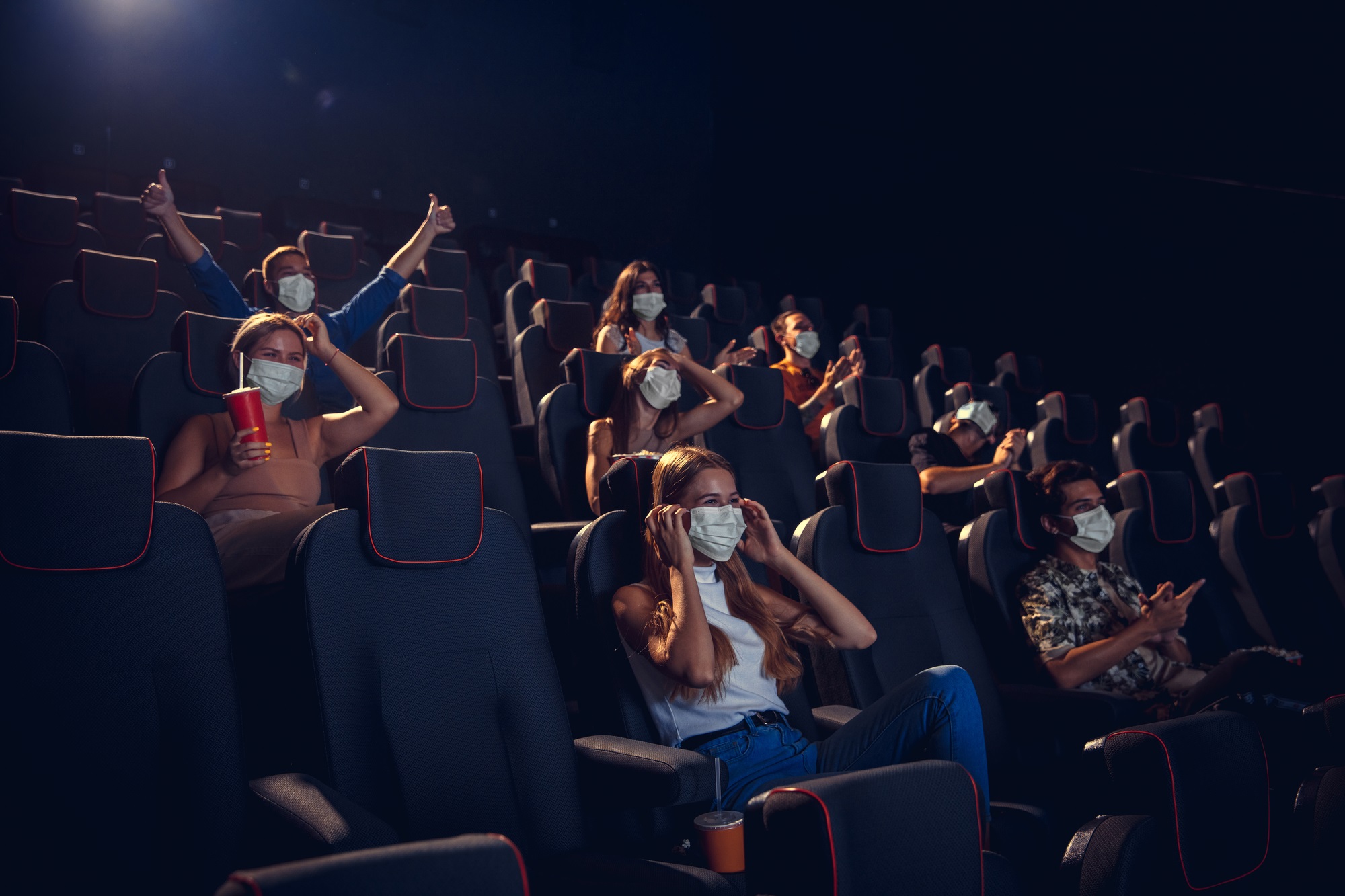 People wearing COVID surgical masks in a dark movie theater