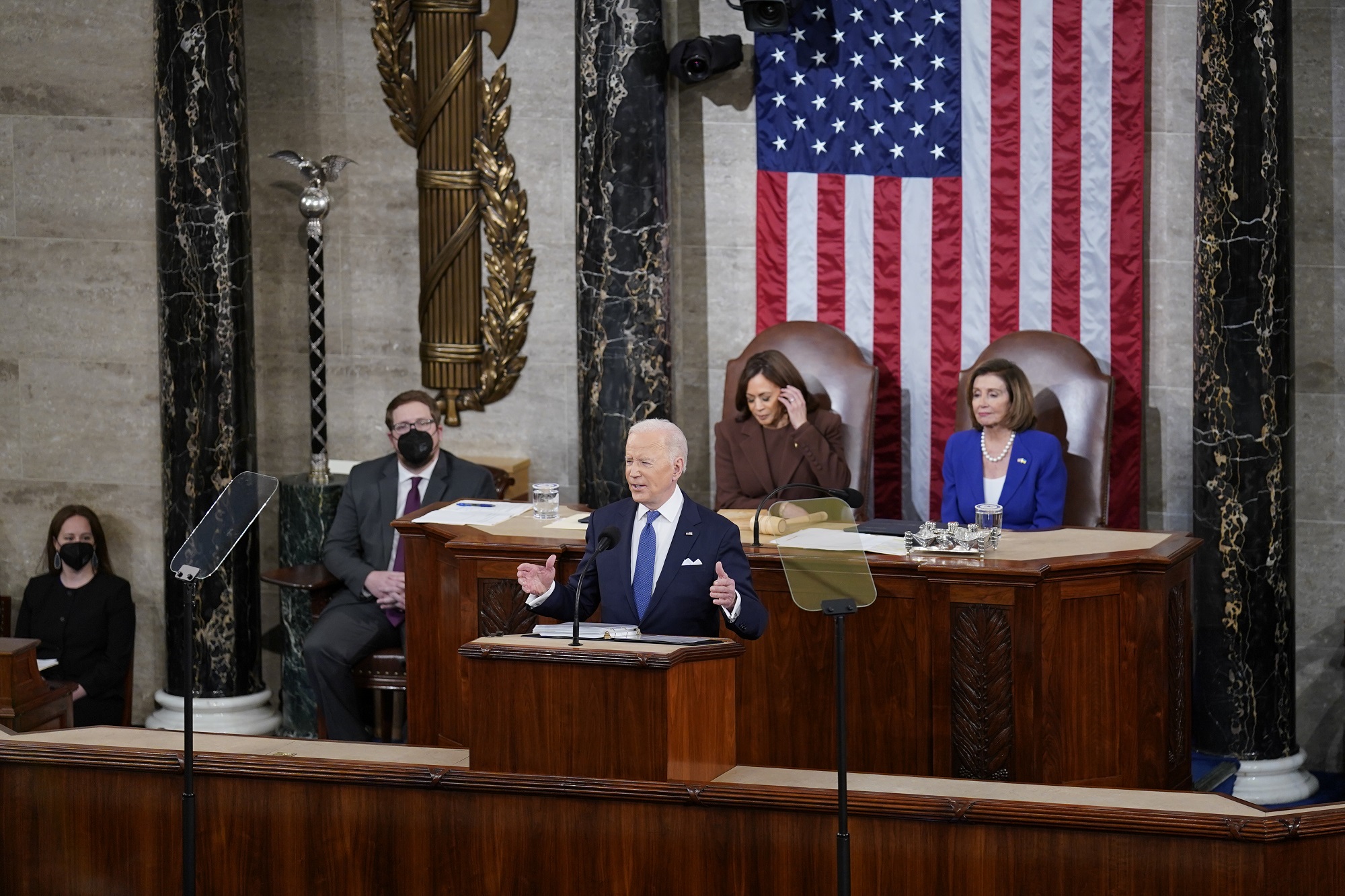 Biden State of the Union 2022 with the US president, vice president, and speaker of the House of Representatives in front of an American flag and two other individuals wearing COVID masks in the Capitol