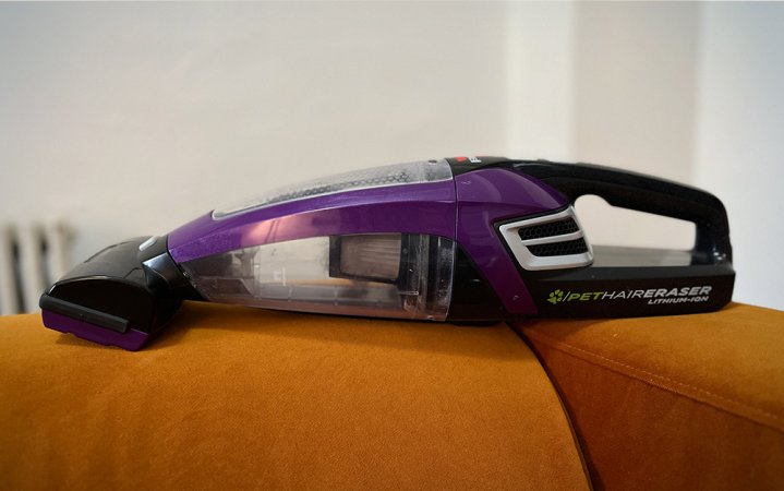  A purple Bissell Pet Hair Eraser Lithium Ion Cordless Hand Vacuum on an orange couch.