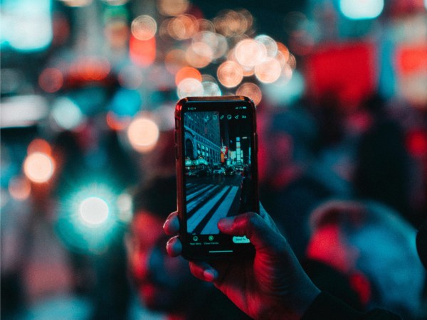 A person holding up their phone in front of a cityscape at night to take a photo for an Instagram Story.