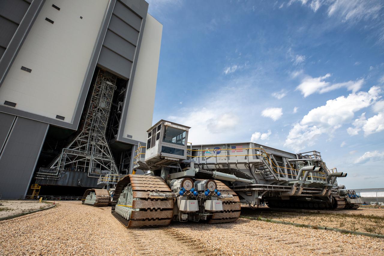 Construction vehicle on treads moving NASA Orion spacecraft parts from a building at Kennedy Space Center in Florida