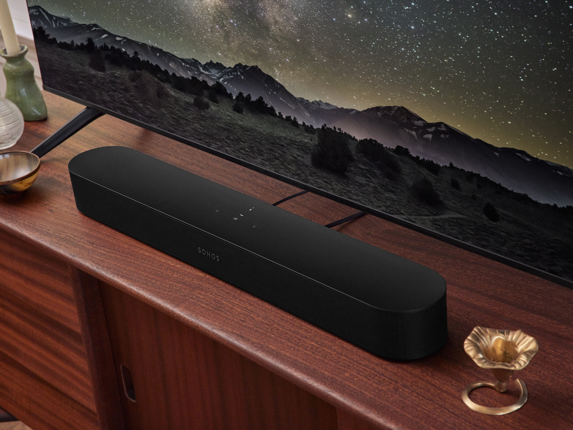 A black Sonos Beam (Gen 2) connected to a TV and sitting atop a wooden entertainment console.