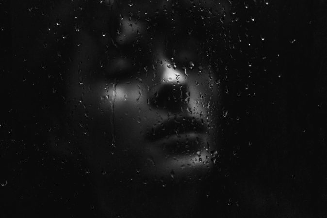 woman in sad mood behind glass with water droplets