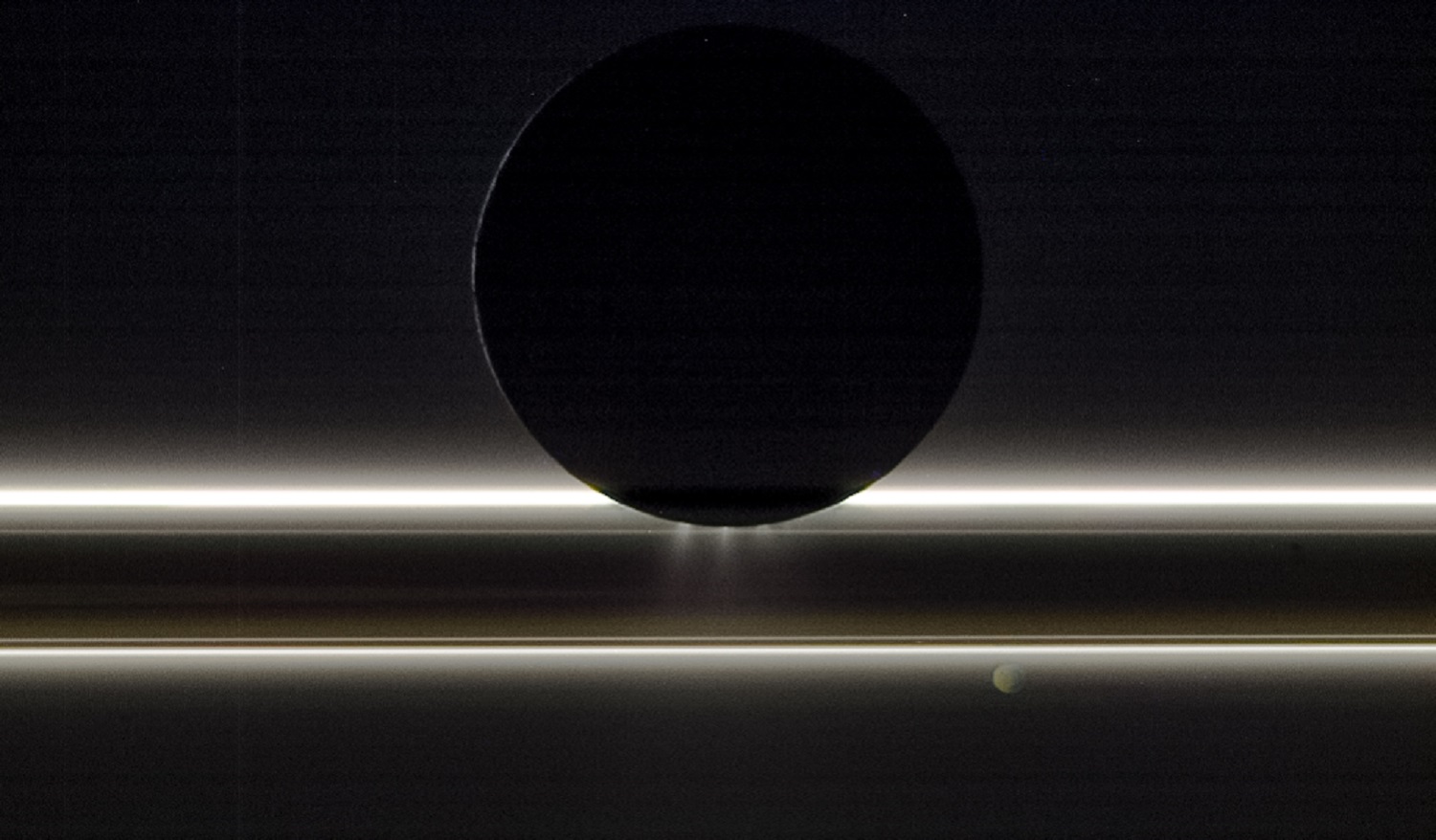 Saturn's moon Enceladus backlit by the sun with jets streaming from the southern end in a space probe image