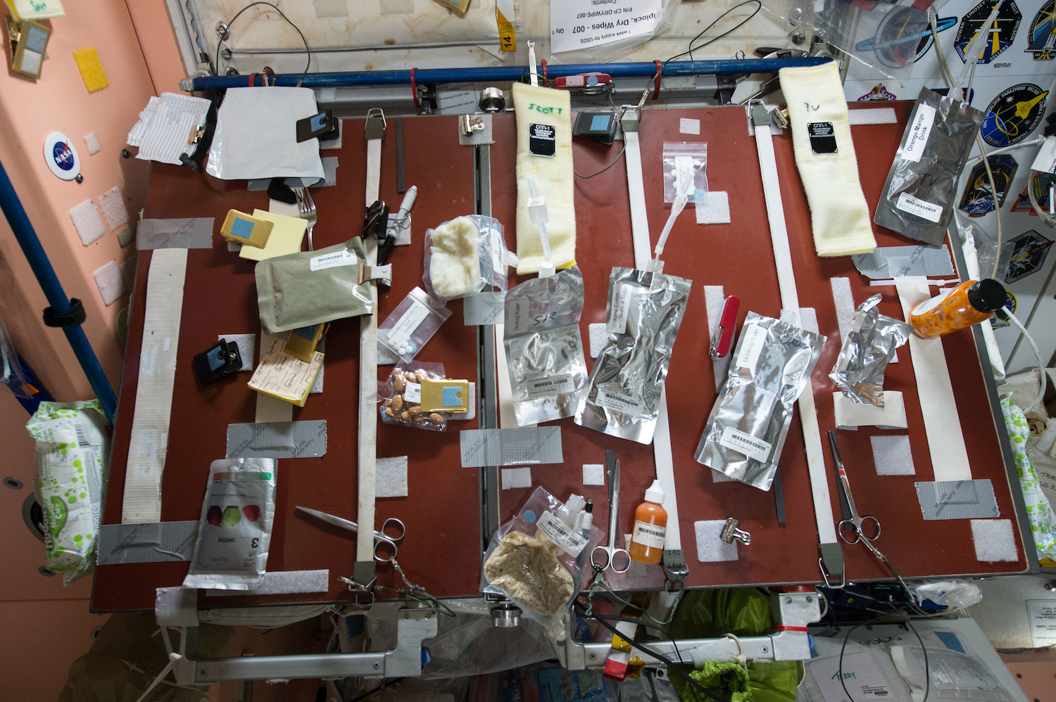 various packets of food, condiments, and drinks are strapped down onto a red table. scissors for cutting packages are also strapped down