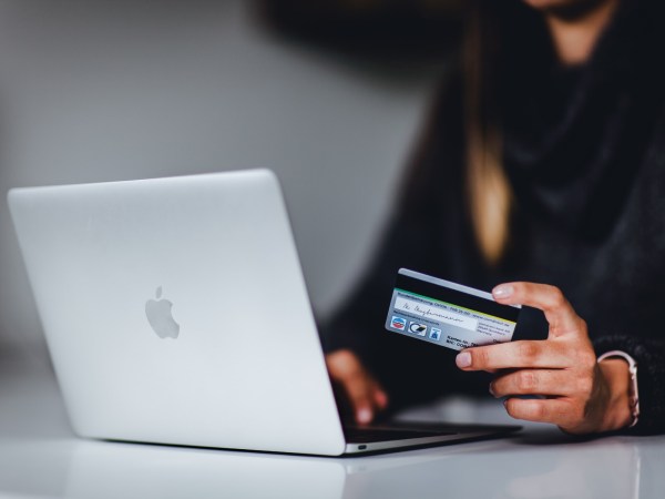 A person sitting in front of a silver Macbook laptop and holding a credit card.