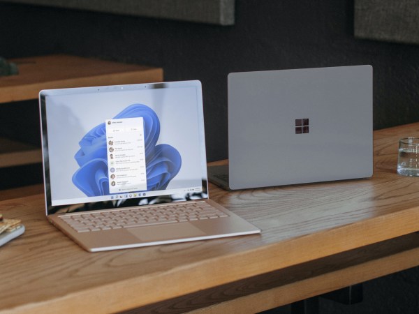 Two Windows laptops on a long wooden table, facing opposite directions. You can see the screen of one, but not the other.