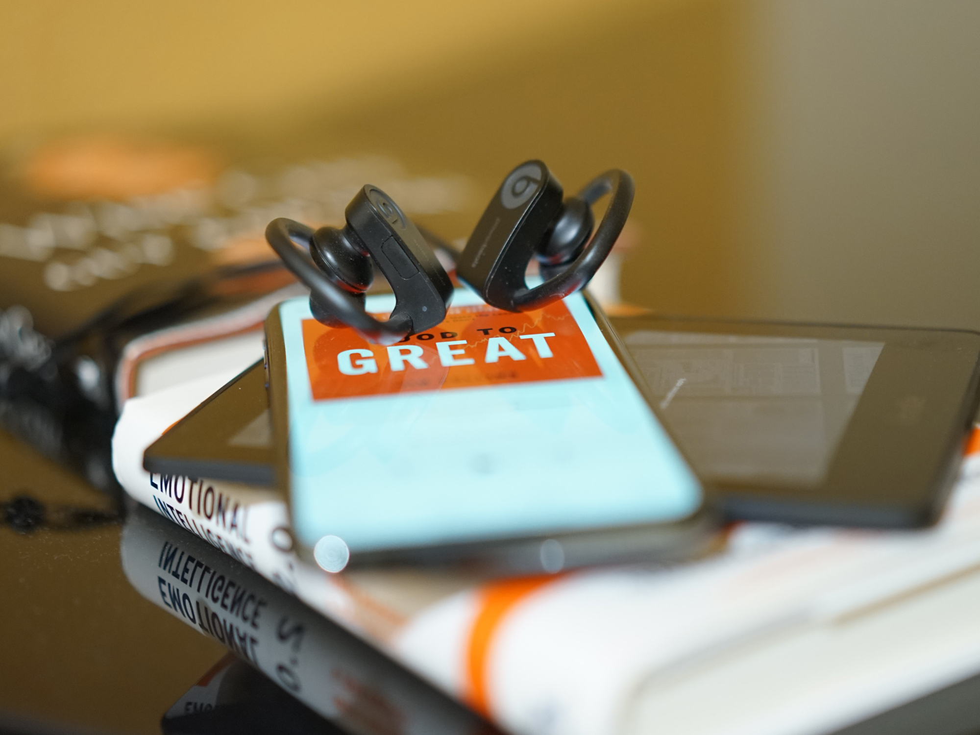 A phone with an audiobook on its screen, sitting on top of an e-reader and an actual book, with some earbuds on top of the phone.