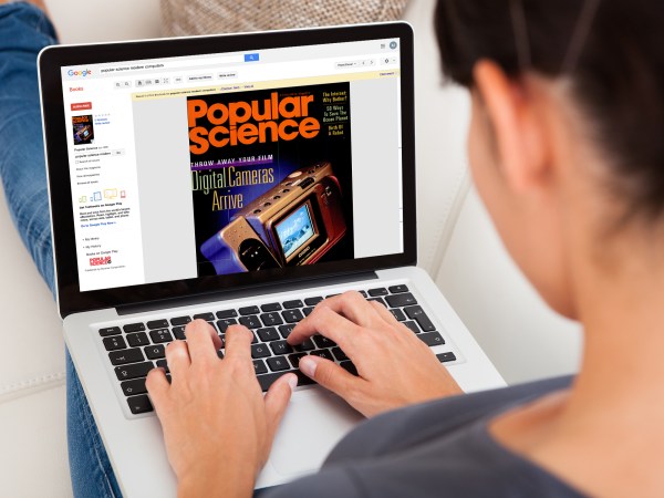 A woman wearing a gray shirt and blue jeans using a laptop on her lap with the Popular Science archive on the screen.