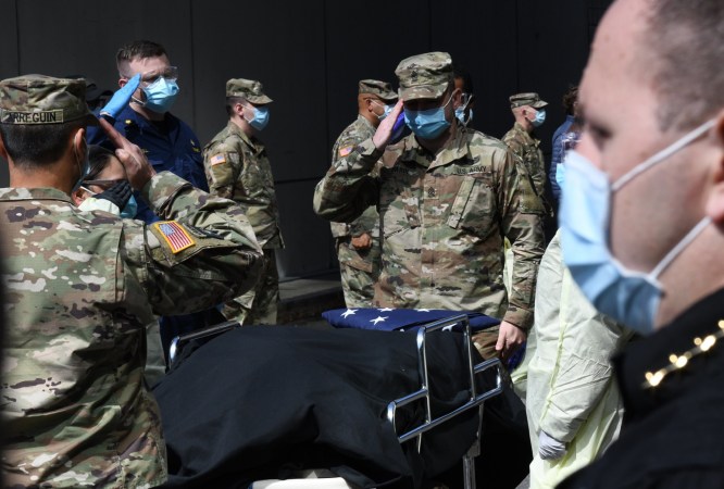 US Army service members in surgical masks saluting the coffin of a veteran who died of COVID-19