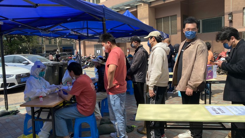 A line of people queue up in front of a blue tent.