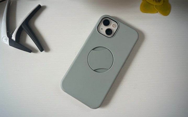  A sage green OtterGrip phone case on white desk near a guitar capo and a pile of yellow guitar picks