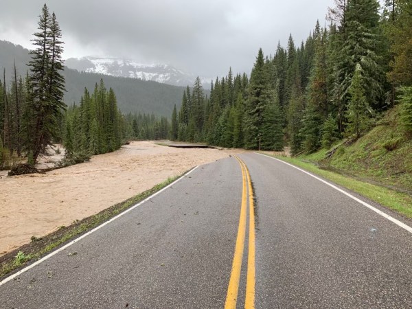 a road in yellowstone park that has murky brown flood water covering part of it, blocking entrance to the park