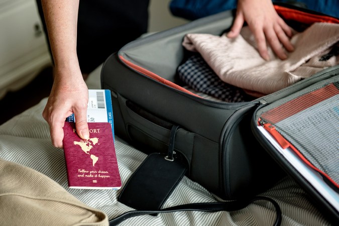 A person packing clothes and a passport into a suitcase