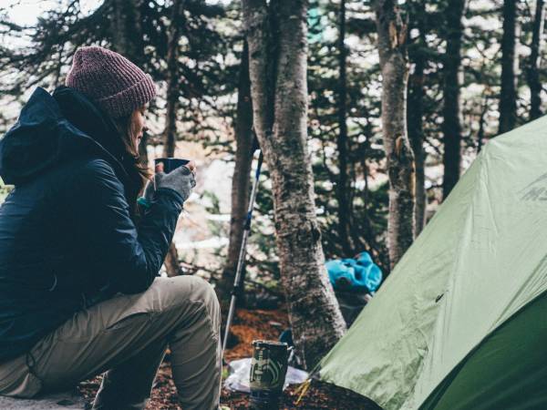 person enjoying a hot beverage by a campsite