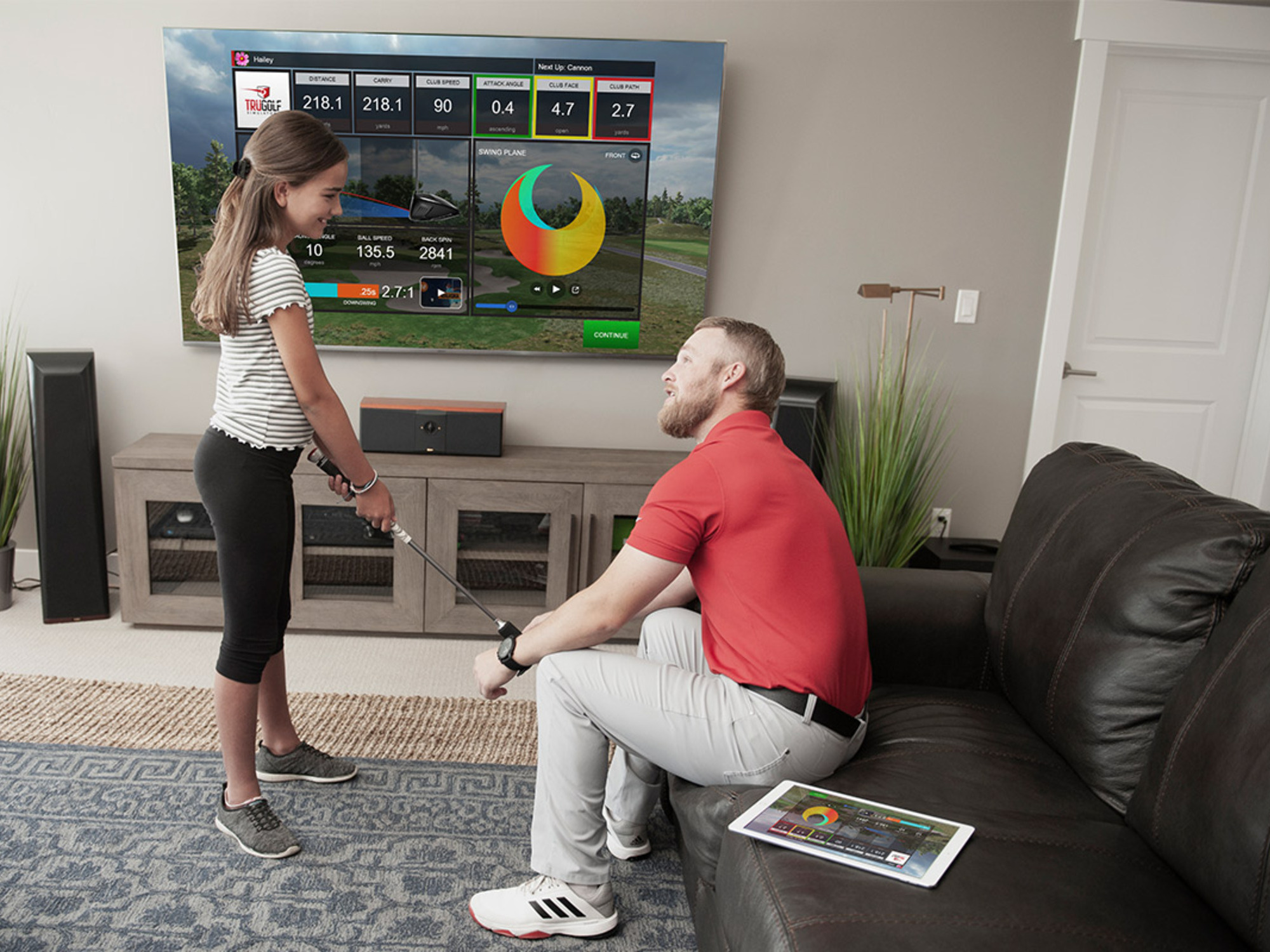 A man sits on a couch and teaches a woman to golf.