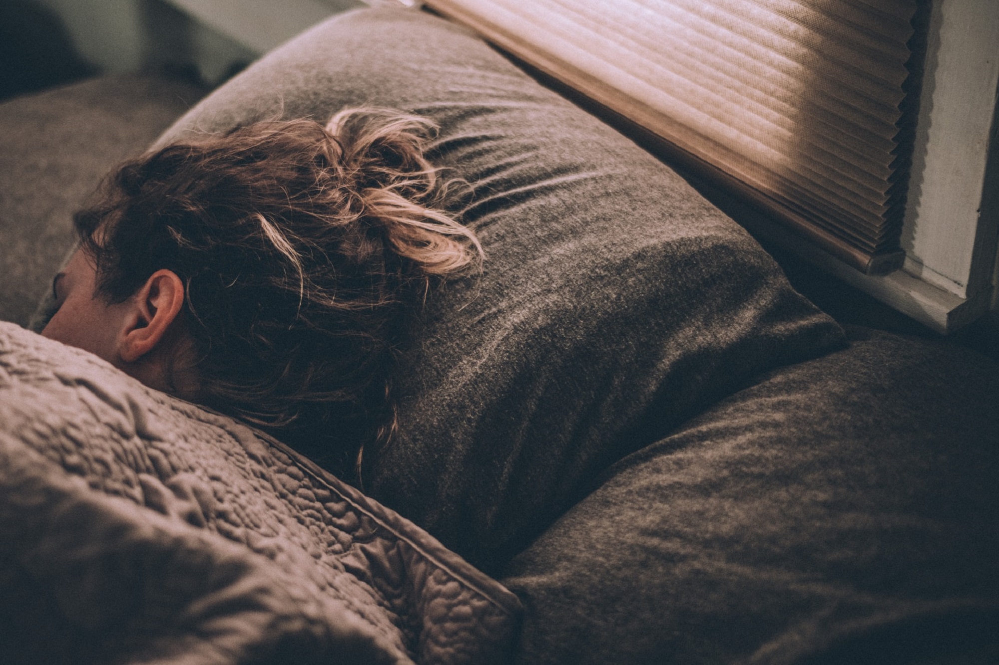 Person with long brown hair sleeping on gray pillows after taking a melatonin supplement