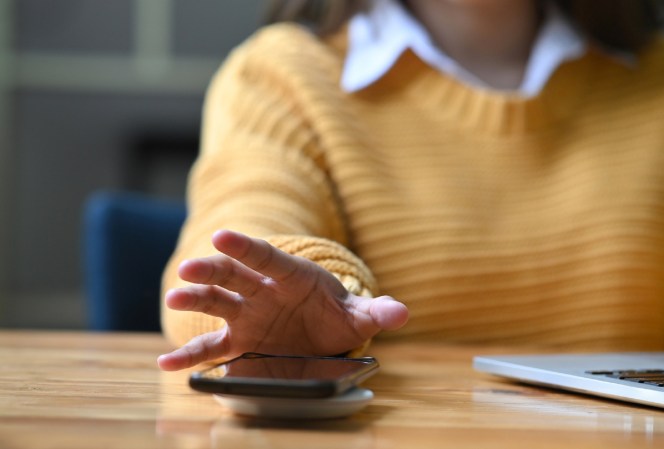 Person in yellow sweater at laptop reaching for a smartphone to call a crisis and suicide hotline