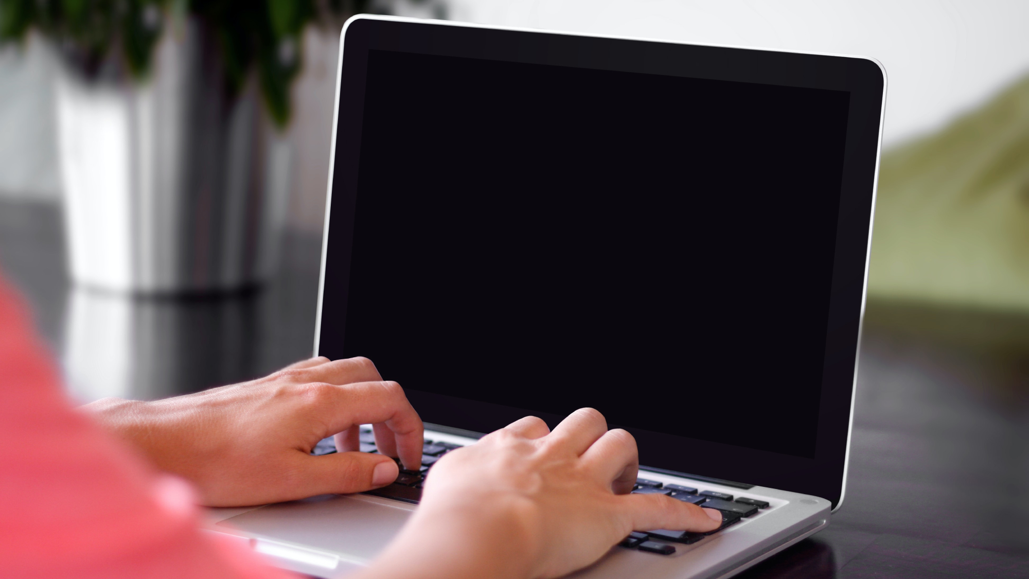 A person in a pink shirt sitting in front of a laptop that has powered off and has a black screen.