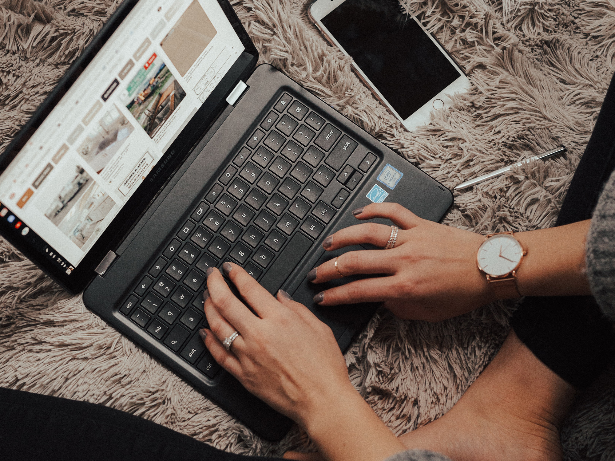 hands on keyboard of laptop with phone beside it