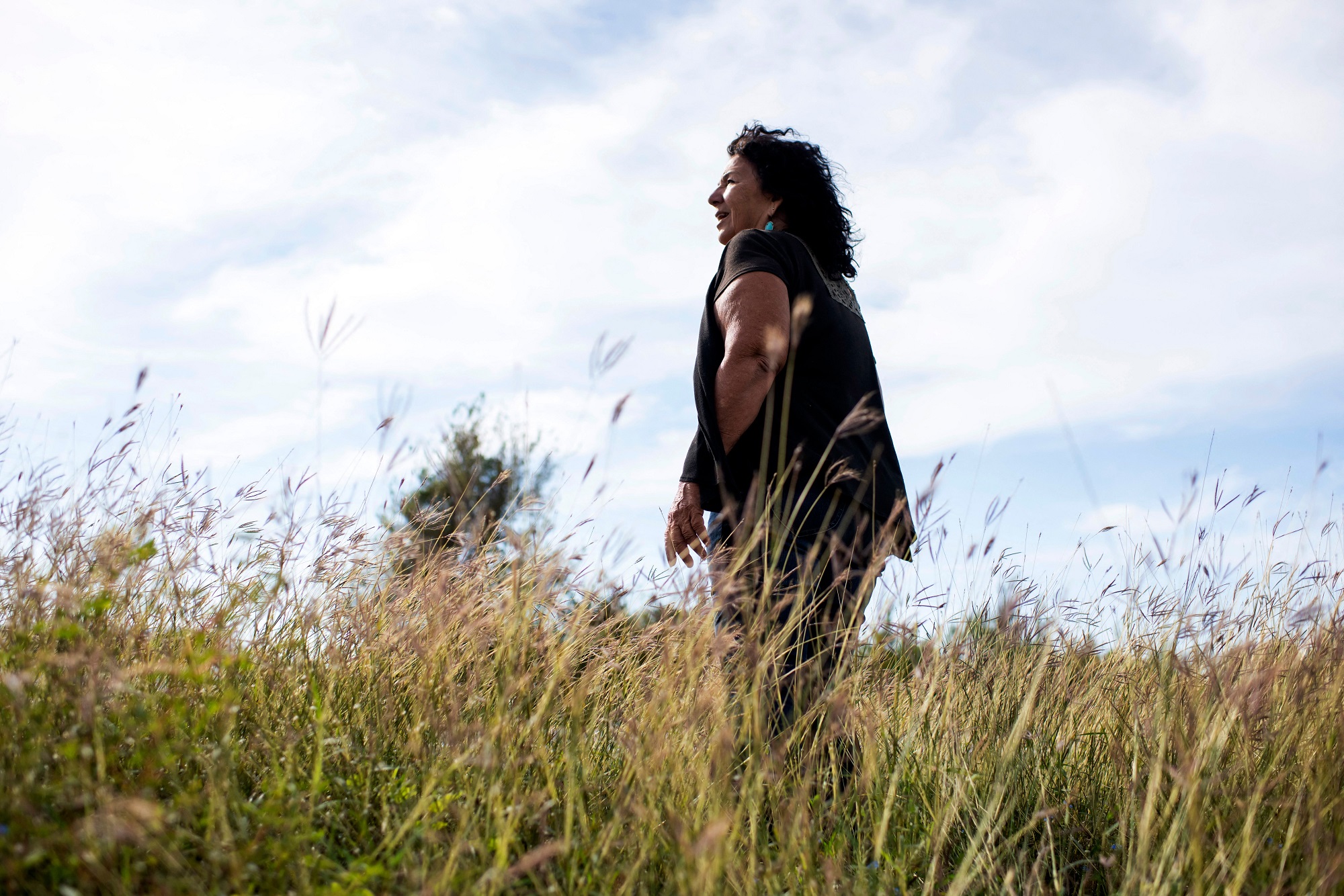 Woman in black shirt and green plants standing in a grassy marsh in front of white clouds by the Formosa plant in Point Comfort, Texas