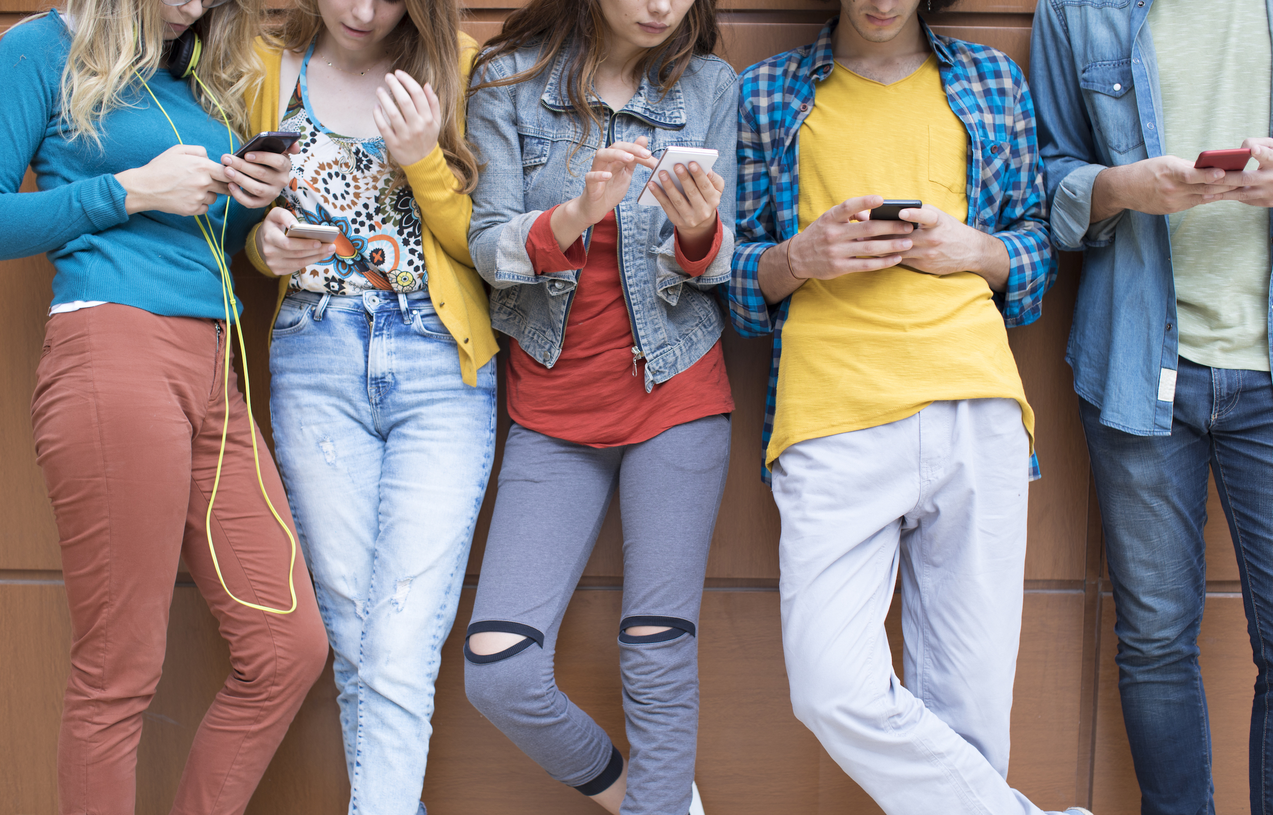 Four teens standing in a row using their smartphones