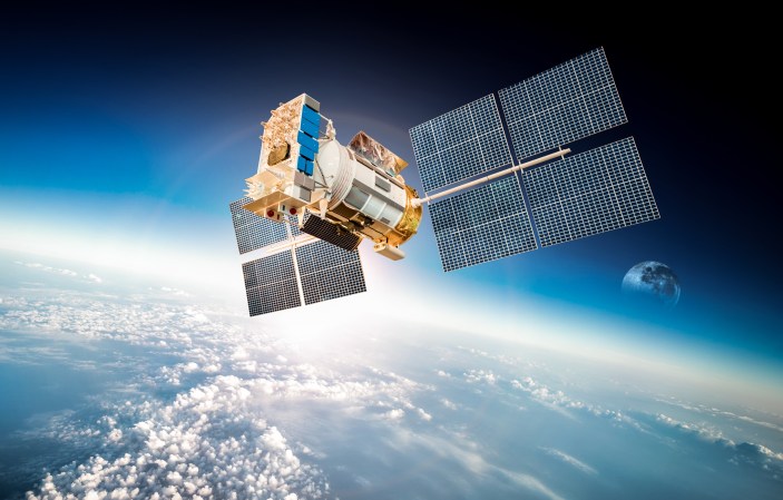 Stock image of a satellite orbiting above the Earth with the moon in the background