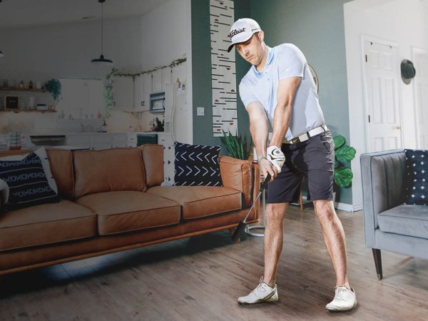 A man dressed in gold gear using a golf simulator to play golf at home